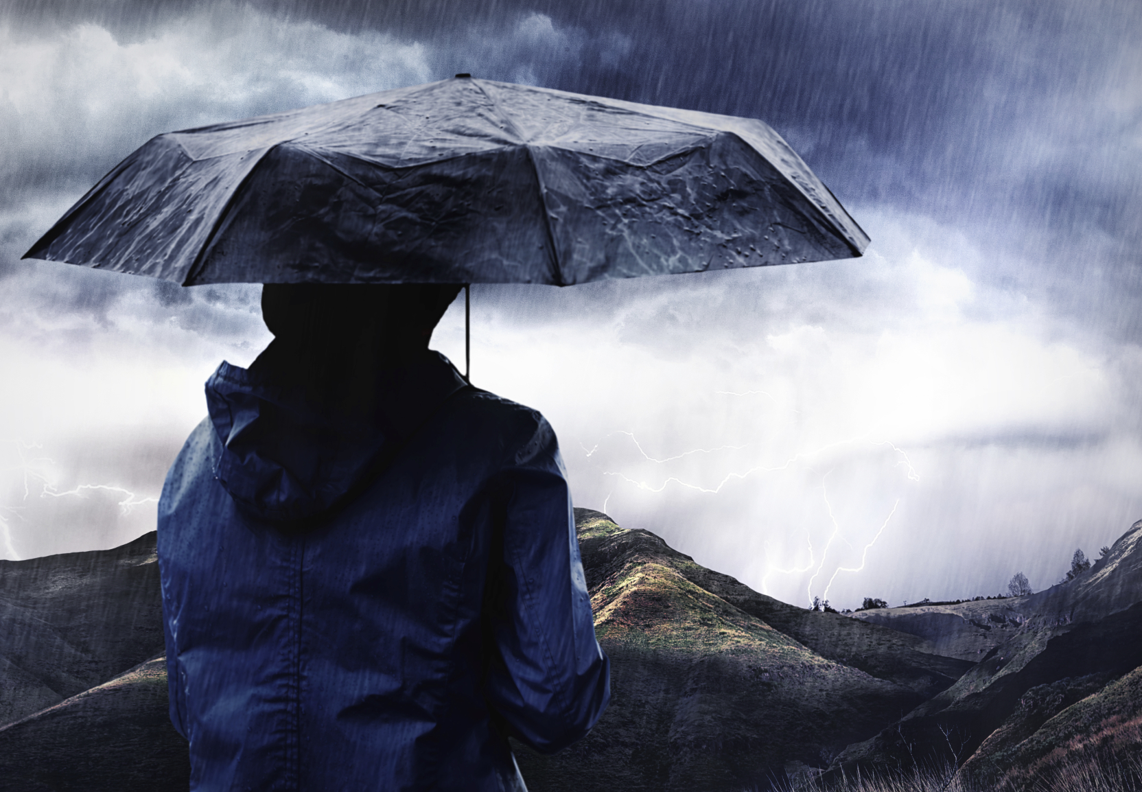 Shot of a woman covered with an umbrella watching a thunderstorm over a mountain