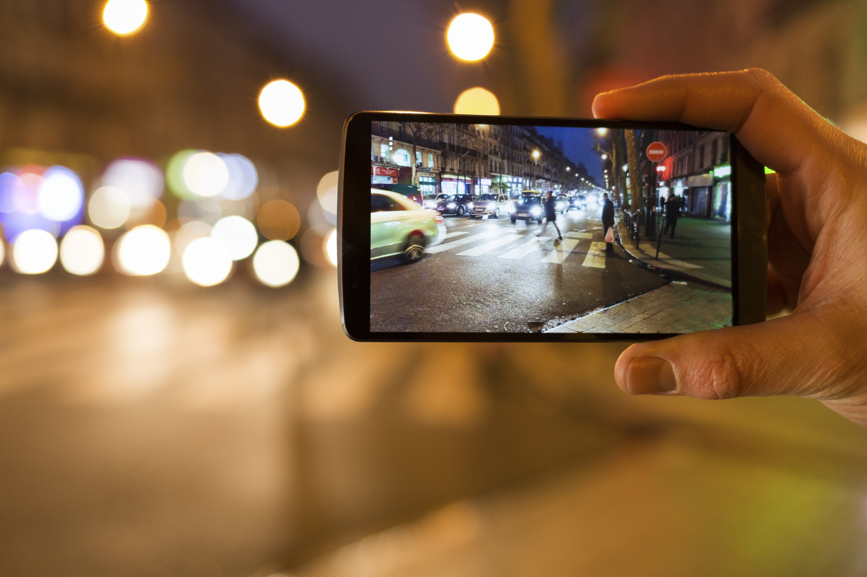 Man makes a picture in the street with his mobile phone. Night light bokeh background