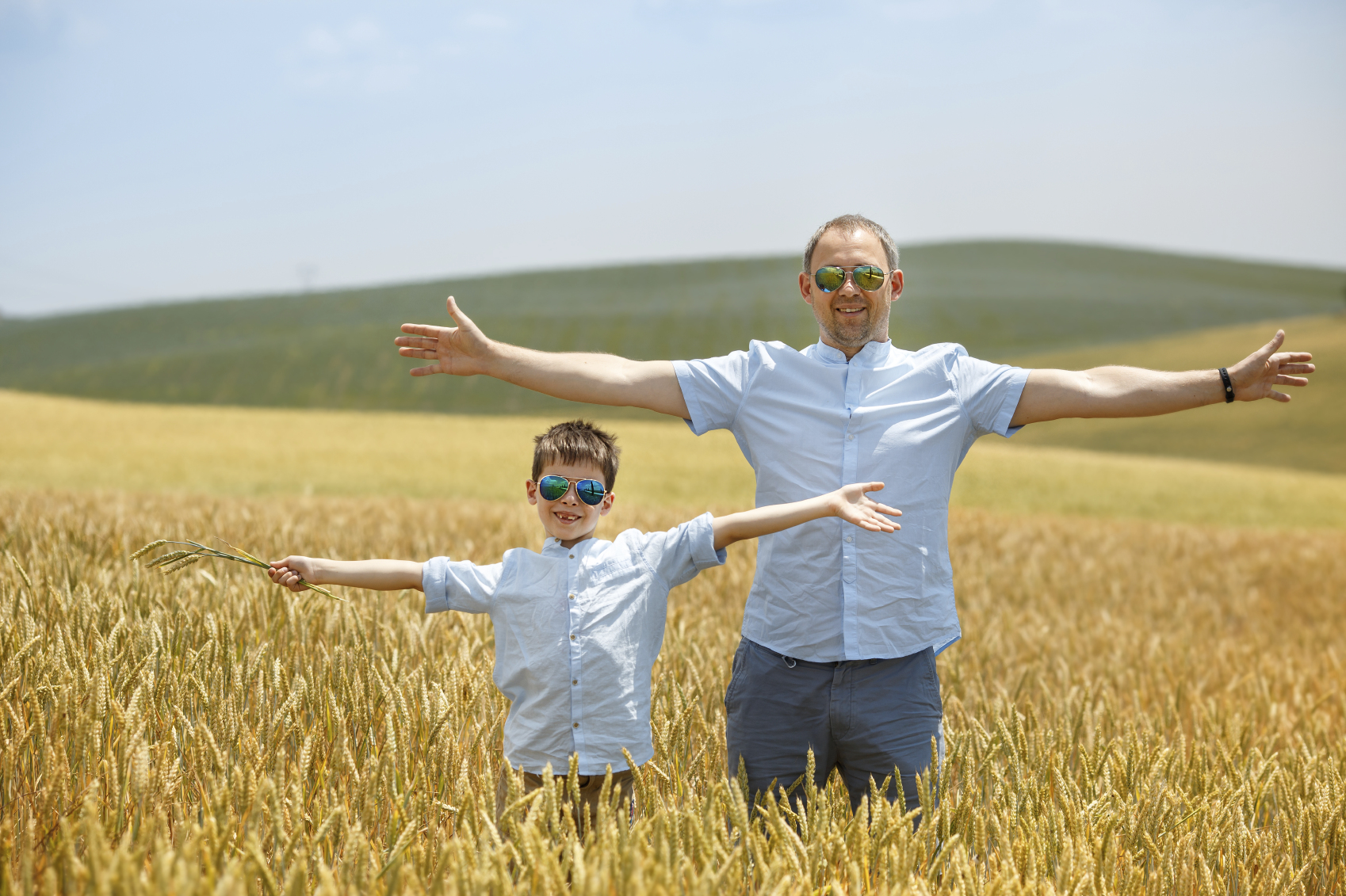 Happy father with little son walking happily in wheat field on warm and sunny summer day
