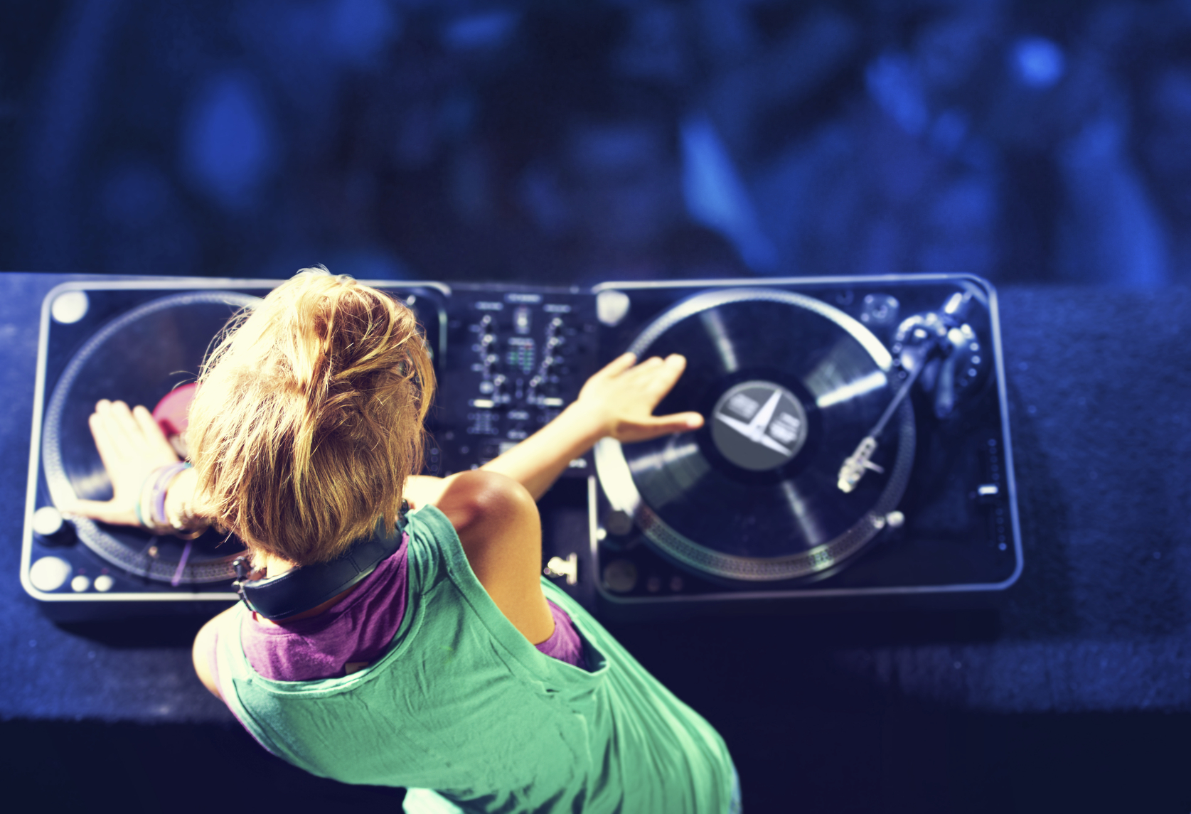 Rear-view shot of a trendy young DJ mixing up some music with a crowd in the background