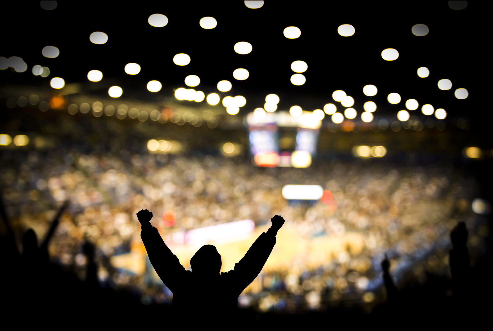 Fans excited at basketball game. Silhouetted fans raising arms in celebration at a basketball game.