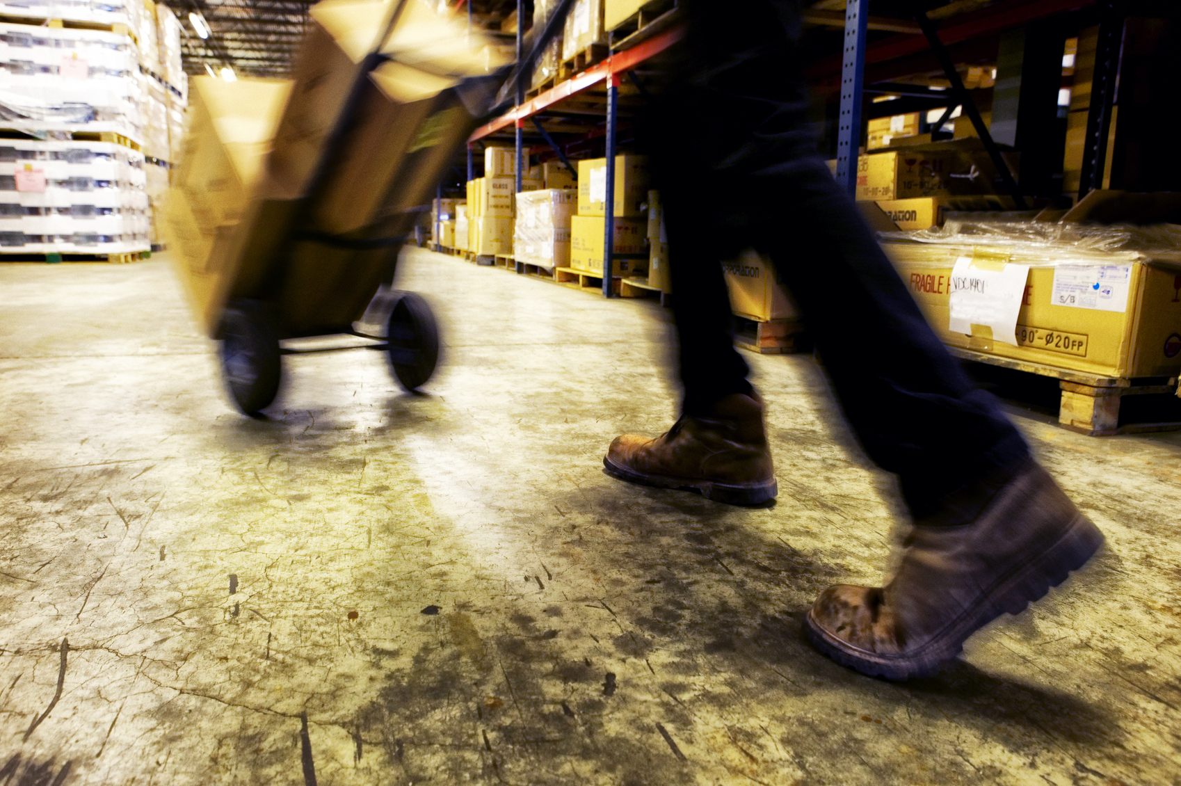 A warehouse worker moving a shipment of boxes using a hand truck.