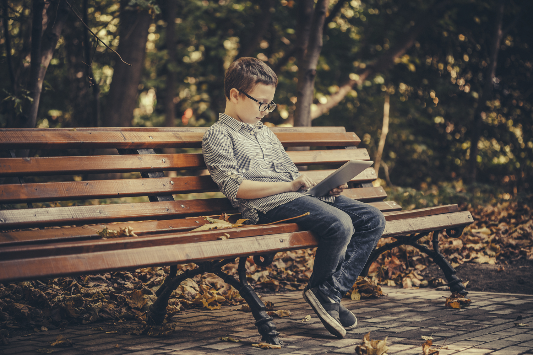 Cute boy using a digital tablet sitting in the park. Stock photo.